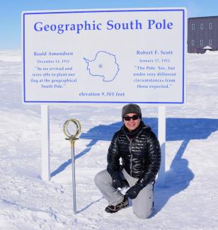 Howard Hui sits underneath a sign that says "Geographic South Pole" 